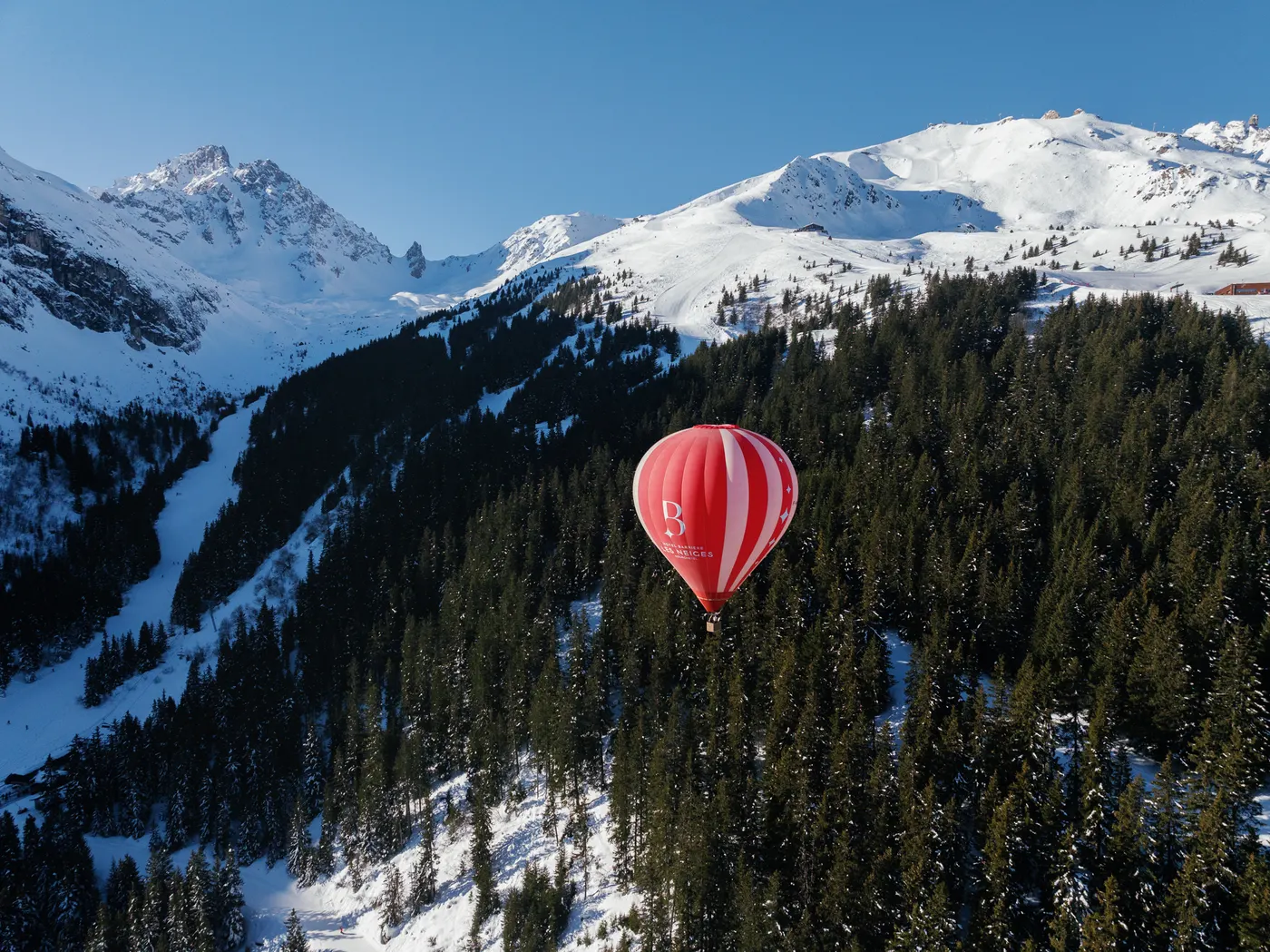 Les Neiges hot air balloon flying above the snowy mountains and forests of Courchevel.