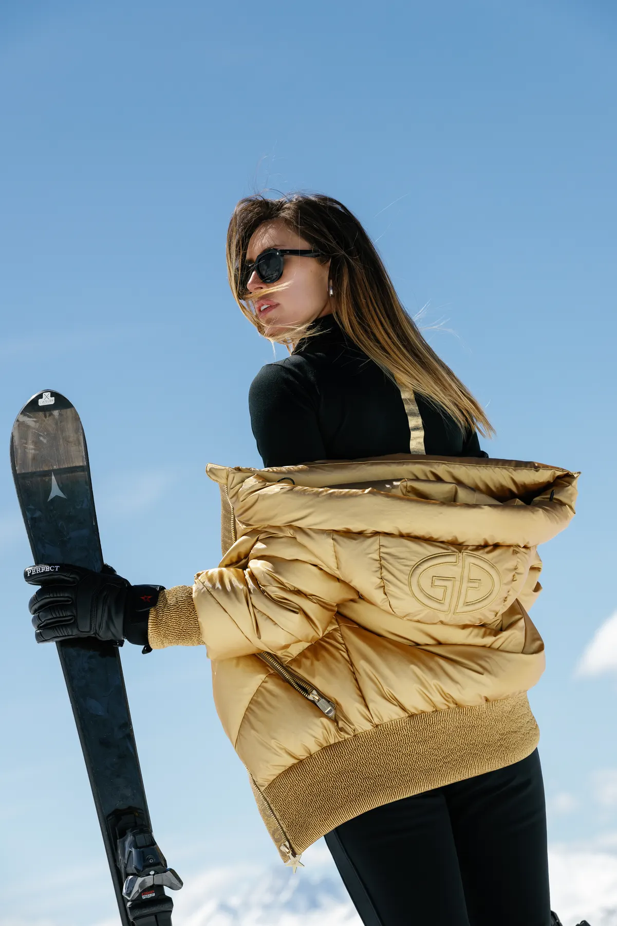 Woman wearing a gold Goldbergh ski jacket posing with skis in Courchevel.