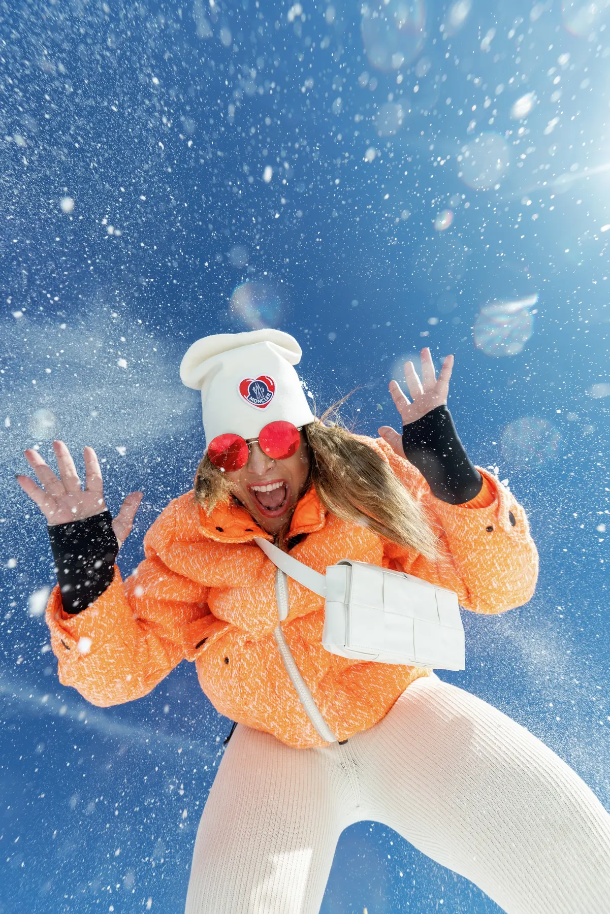 Woman wearing an orange Moncler ski jacket playing in the snow in Courchevel.