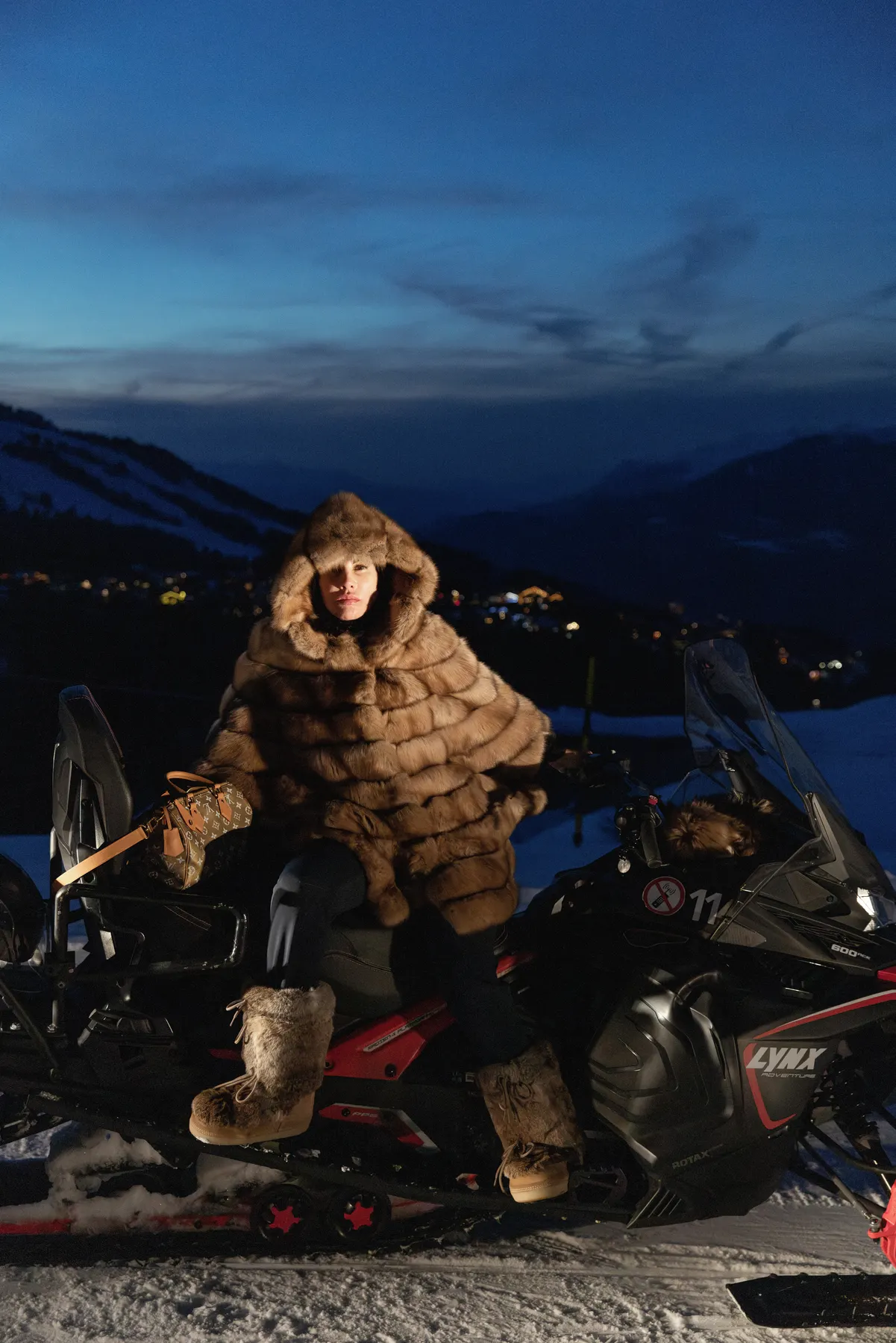 Woman wearing a fur jacket posing on a snowmobile during an evening experience in Courchevel.