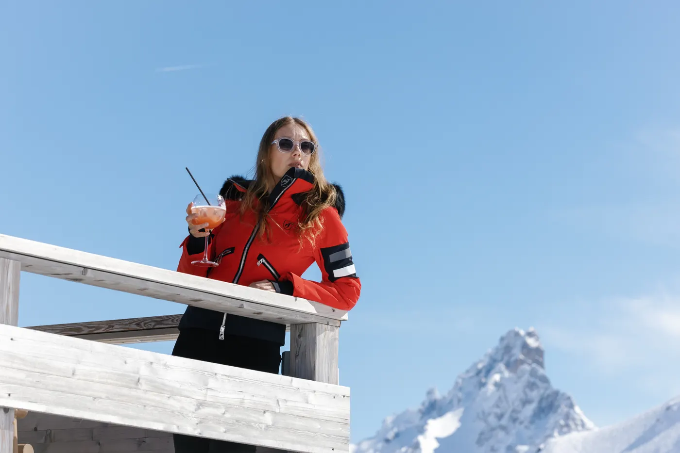 Woman wearing a red Toni Sailer ski jacket enjoying après-ski with a drink in Courchevel.