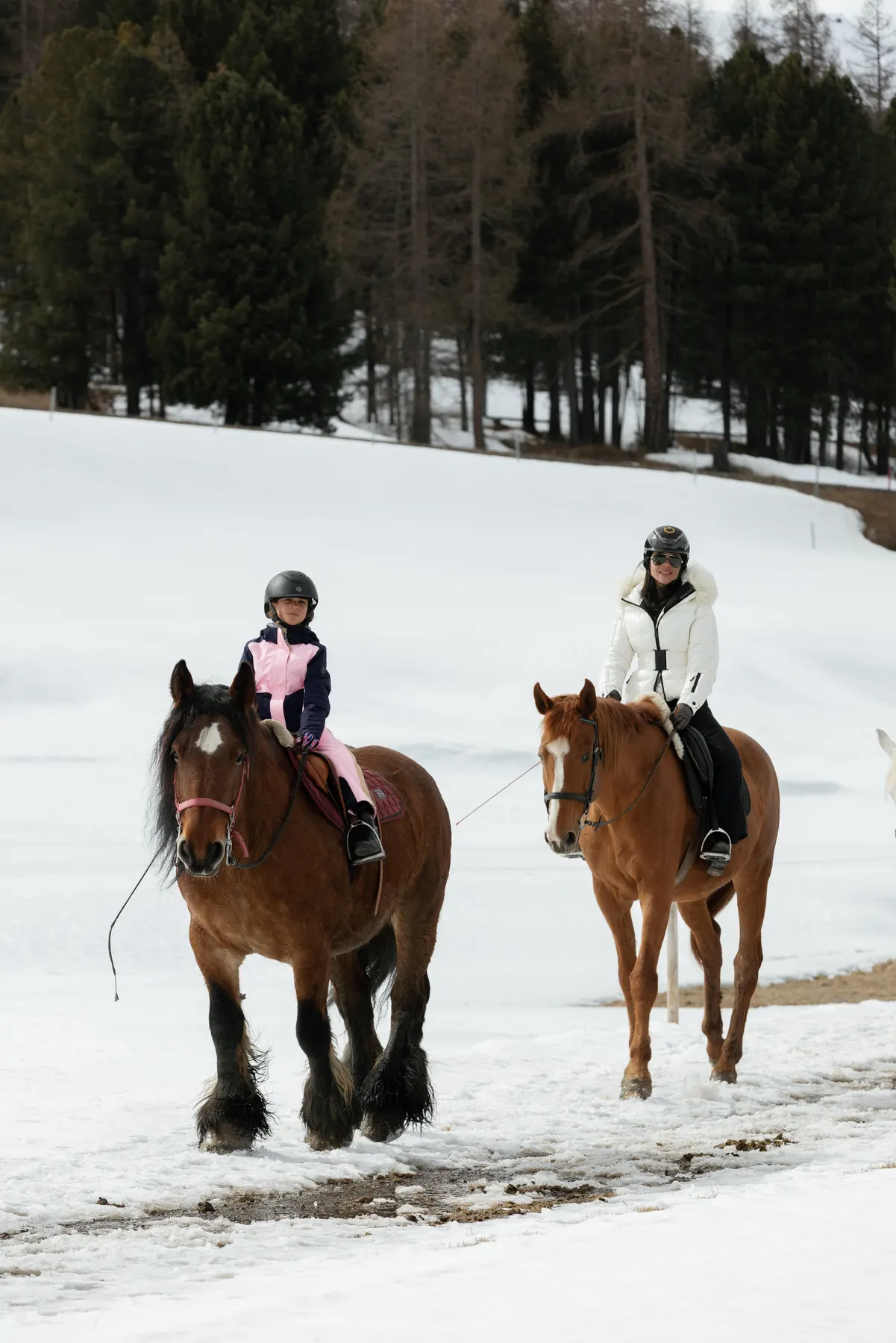 Mother and daughter horse riding through the snow during a winter holiday in St. Moritz.